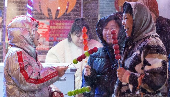 Mujeres compran fruta acaramelada en una calle de Shenyang, China, en la víspera del Año Nuevo lunar. - Sputnik Mundo