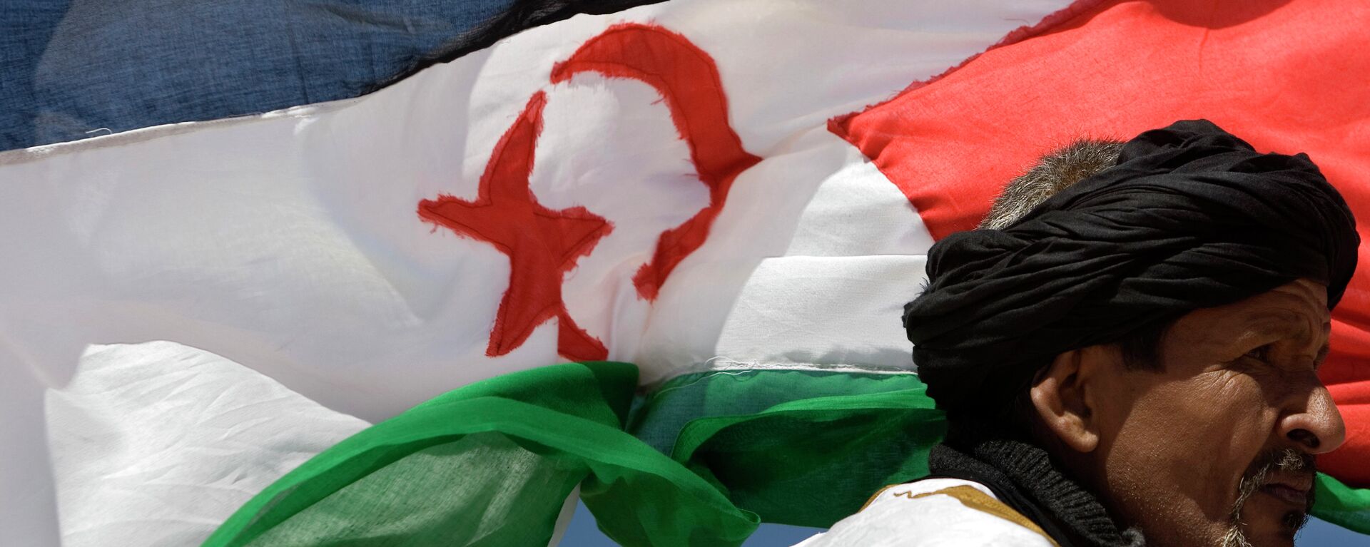 A pro-independence Polisario Front supporter looks on during a military parade as a Western Sahara flag flies in the breeze in the village of Tifariti - Sputnik Mundo, 1920, 13.12.2020