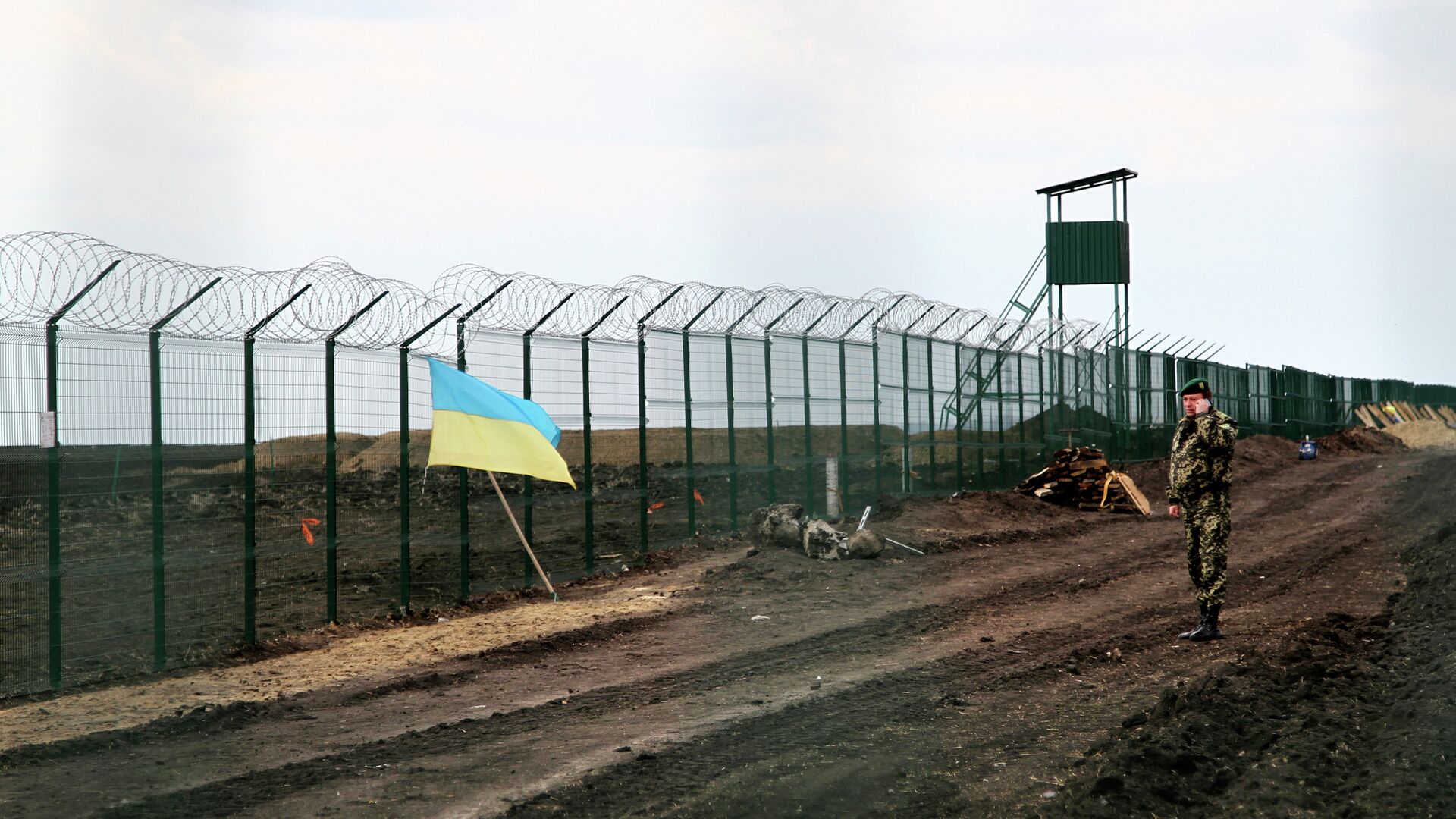 A Ukrainian border guard officer speaks on a phone near a national flag attached to the fence on the Ukrainian-Russian border near Hoptivka, Kharkiv region, eastern Ukraine - Sputnik Mundo, 1920, 06.12.2021