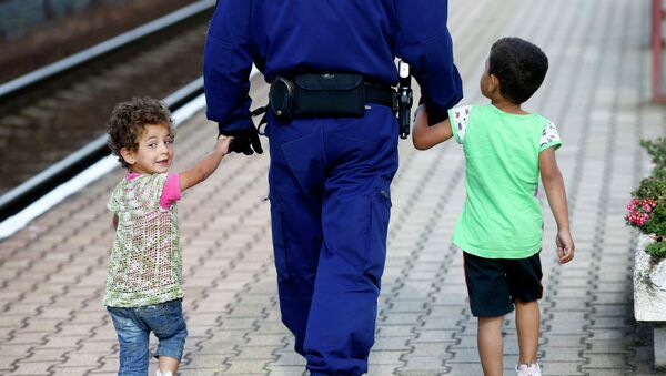 A police officer escorts migrant children along a platform to a waiting train bound for Munich, at the railway station in Hegyeshalom, Hungary - Sputnik Mundo
