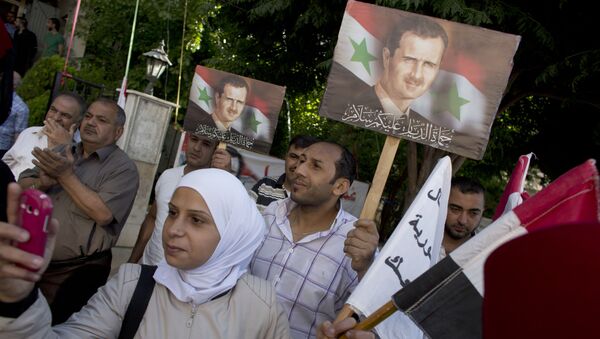 La gente tiene retratos del presidente sirio Bashar Assad fuera de un centro de votación en Damasco - Sputnik Mundo