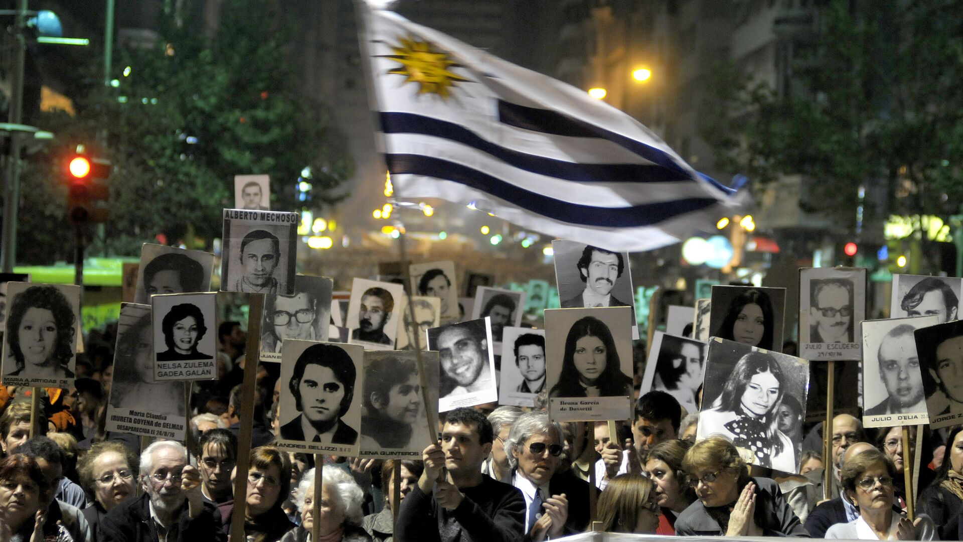 Demonstrators, one waving an Uruguayan flag, carry signs with images of people missing during Uruguay's 1973-85 dictatorship during a march in Montevideo, Uruguay - Sputnik Mundo, 1920, 04.05.2023