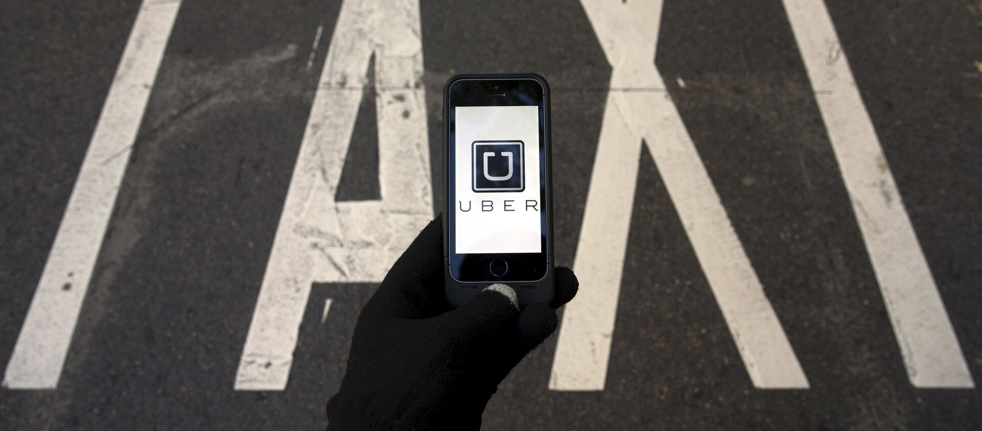 The logo of car-sharing service app Uber on a smartphone over a reserved lane for taxis in a street is seen in this file photo illustration taken in Madrid on December 10, 2014 - Sputnik Mundo, 1920, 02.02.2020