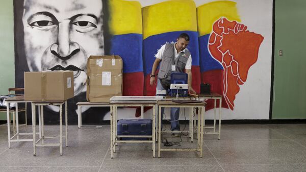 A worker of the National Electoral Council (CNE) configures a voting machine in front of a mural depicting Venezuela's late President Hugo Chavez at a school in Caracas, December 4, 2015. Venezuela will hold parliamentary elections on December 6. - Sputnik Mundo
