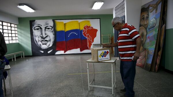 A man deposits his vote in a ballot box near a painting of Venezuela's late President Hugo Chavez during a legislative election, in Caracas - Sputnik Mundo