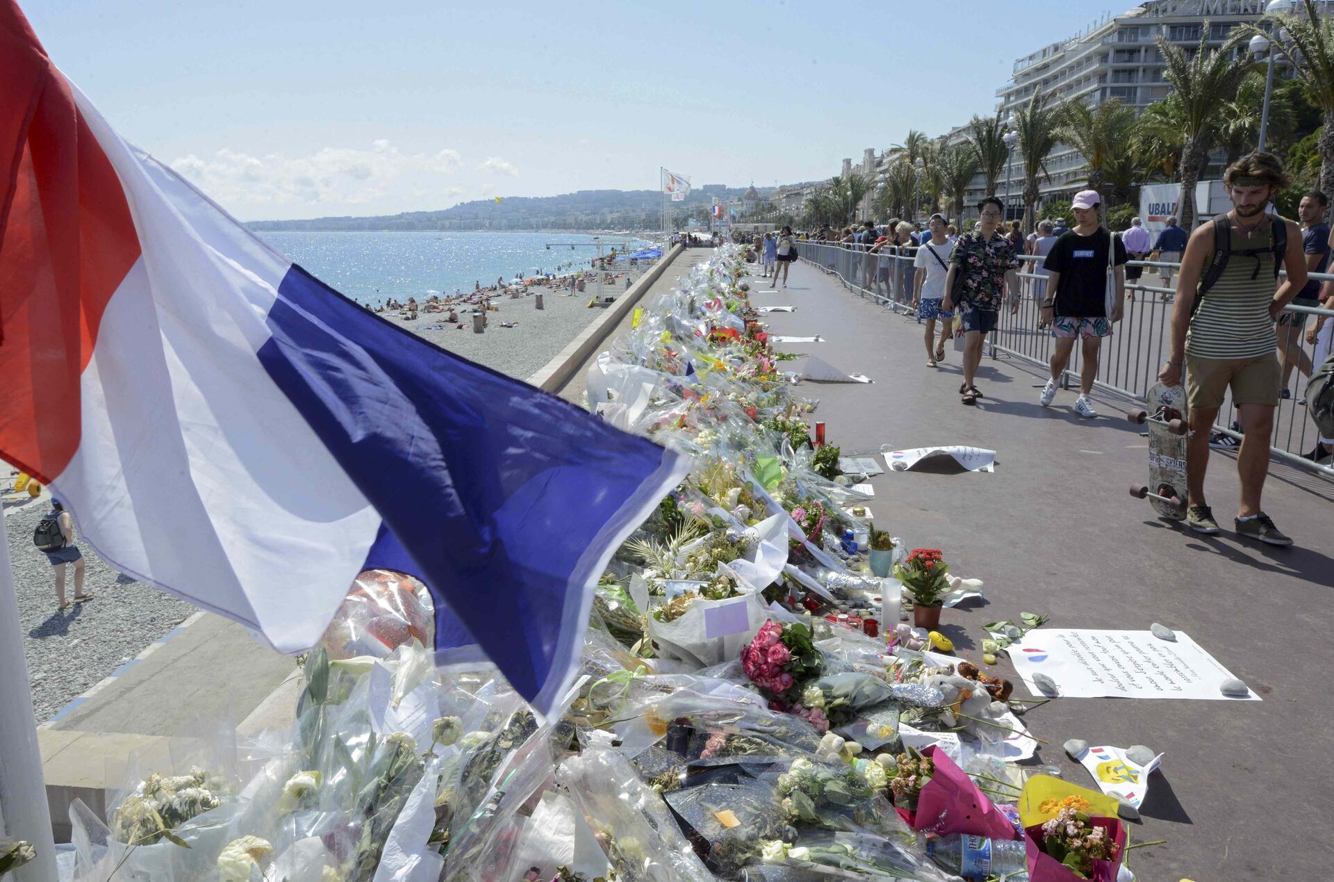 People walk past flowers left in tribute at a makeshift memorial to the victims of the Bastille Day truck attack near the Promenade des Anglais in Nice - Sputnik Mundo, 1920, 11.03.2021