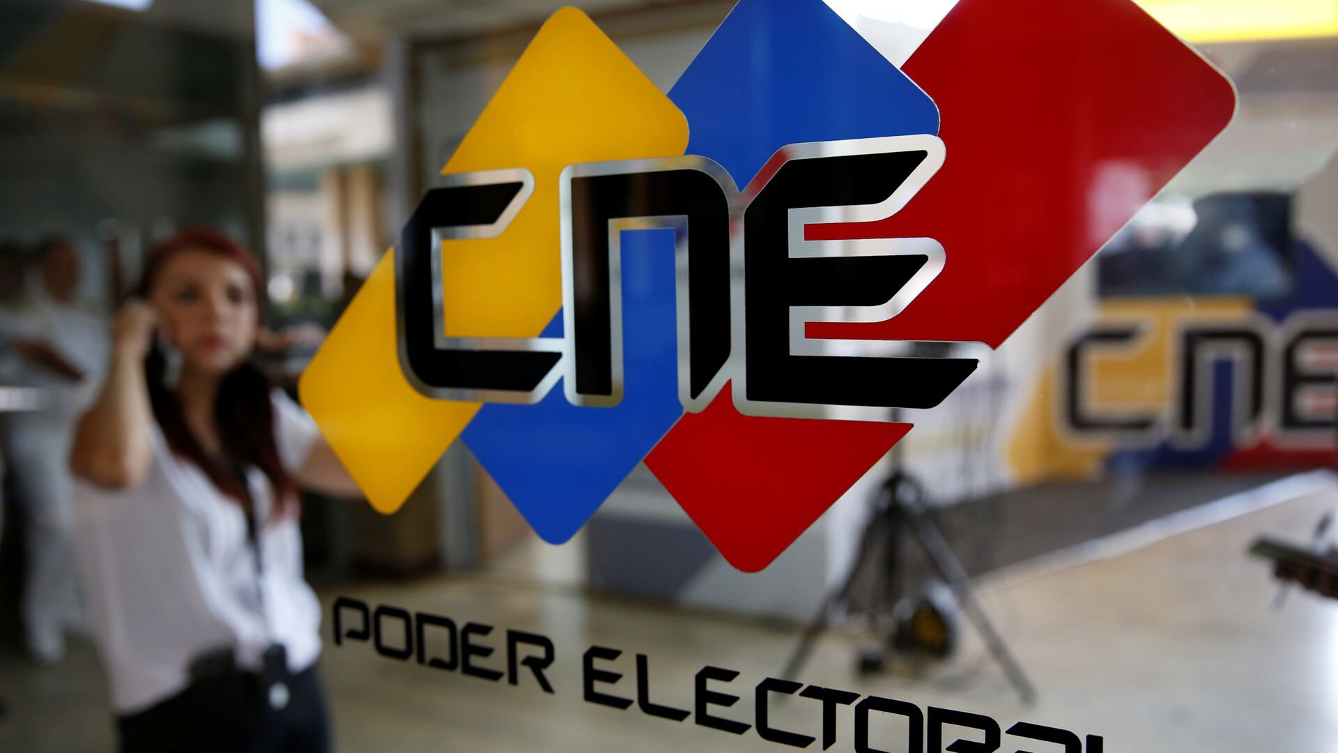 People walk past a logo of the National Electoral Council (CNE) at its headquarters in Caracas - Sputnik Mundo, 1920, 09.08.2021