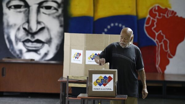 Un venezolano está votando en las elecciones presidenciales en Caracas con una imagen del expresidente del país, Hugo Chávez, de fondo - Sputnik Mundo