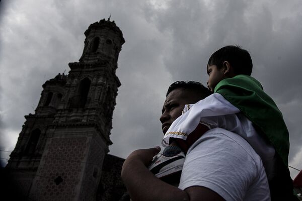 Padre carga a su hijo vestido como San Judas Tadeo frente al Templo de San Hipólito, en la Ciudad de México Padre carga a su hijo vestido como San Judas Tadeo frente al Templo de San Hipólito, en la Ciudad de México - Sputnik Mundo