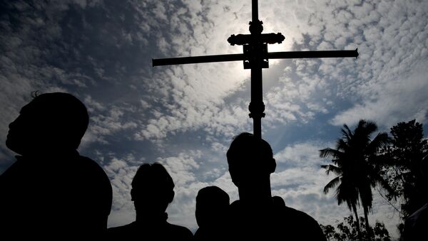 Un hombre sostiene una cruz durante un entierro masivo de víctimas en Sri Lanka - Sputnik Mundo