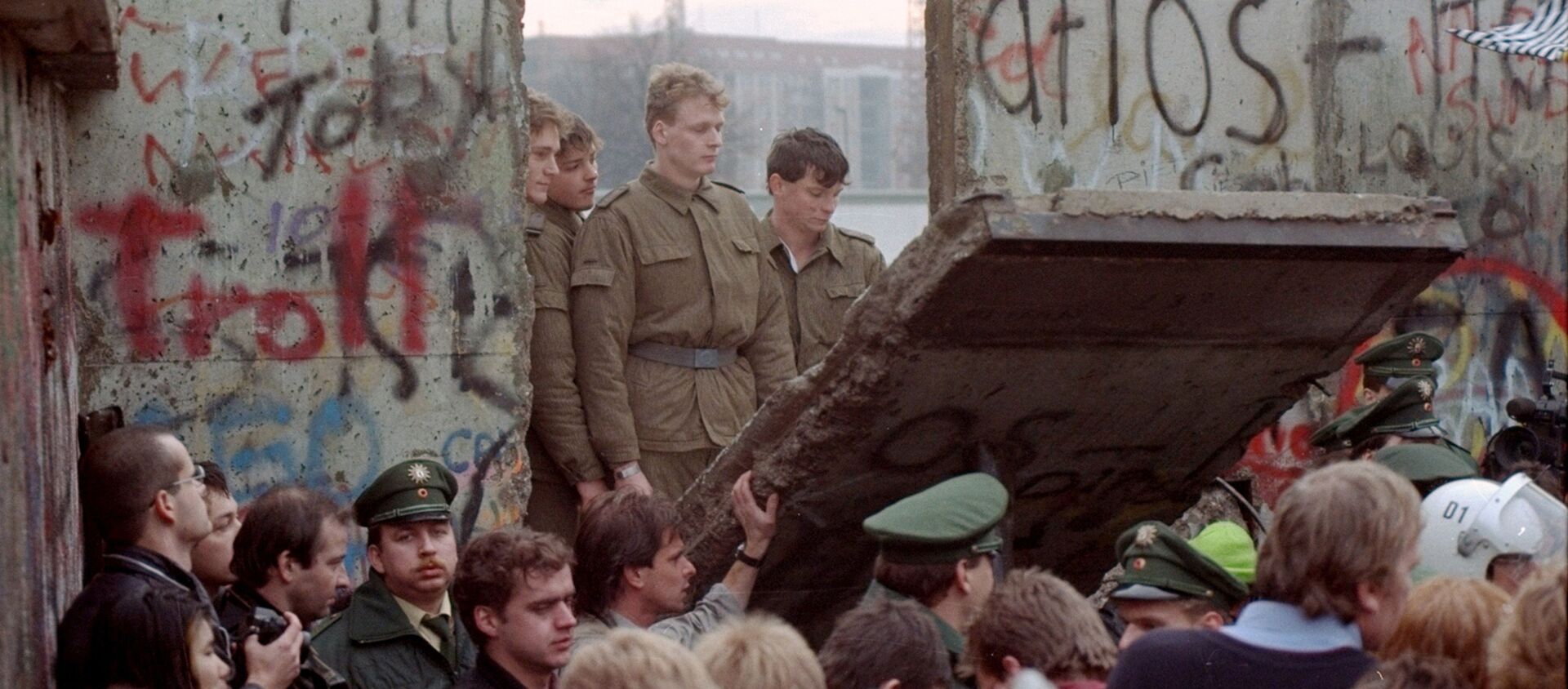 Guardias fronterizos de Alemania Oriental aparecen tras el muro de Berlín después que los manifestantes derribaron un segmento  - Sputnik Mundo, 1920, 08.11.2019