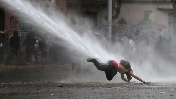 Un manifestante cae al suelo por un tanque de agua durante las protestas en Chile (archivo) - Sputnik Mundo