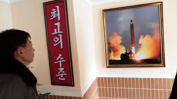 Un hombre mira la foto del lanzamiento de un misil norcoreano - Sputnik Mundo