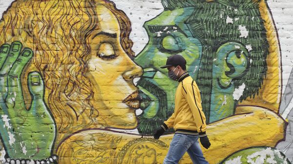 Un hombre en mascarilla pasa al lado de un muro con graffiti en Quito - Sputnik Mundo