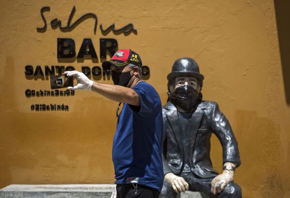 Un hombre con barbijo se toma una selfie en la escultura del cantante español Joaquín Sabina, que también lleva una mascarilla, en Santo Domingo, República Dominicana - Sputnik Mundo